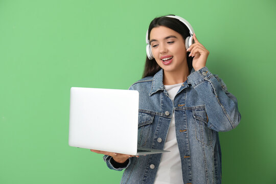 Happy young female programmer in headphones with laptop on green background