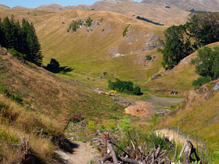 Excavator clearing a path in a rugged rolling hills landscape © mcgimpseymike