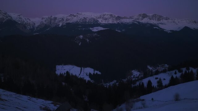 Low altitude aerial pan left reveals traditional barn and pine forest with the stunning western crest of Bucegi and Leaota mountains at dusk