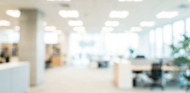 A blurred image of a modern office interior showcasing desks, plants, and bright lighting, creating a professional and inviting atmosphere.