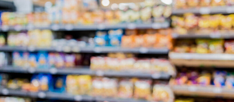 A blurred image of a supermarket aisle filled with various packaged foods on shelves, creating an impression of a busy shopping environment.