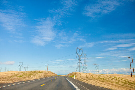 An empty highway winds through fields and under electrical wires