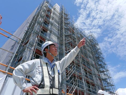 青空の下建設現場で安全ヘルメットの男性作業員が指差し未来を見据えるビジネス