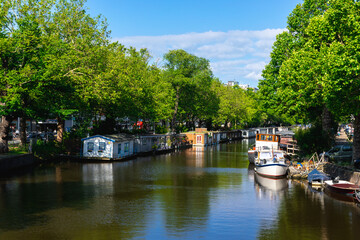 Fototapeta premium Tree-lined canal with houseboats and boats in Amsterdam, Netherlands