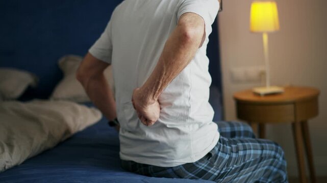 Senior man with backache sitting on bed.
