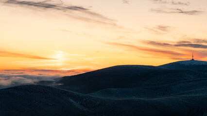 Fototapeta premium Panoramic view at vast winter mountain plains glowing in warm golden sunrise light with deep snow.