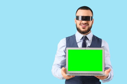 Smiling man in futuristic visor holding laptop with green screen, digital technology and virtual reality concept, business presentation and advertising