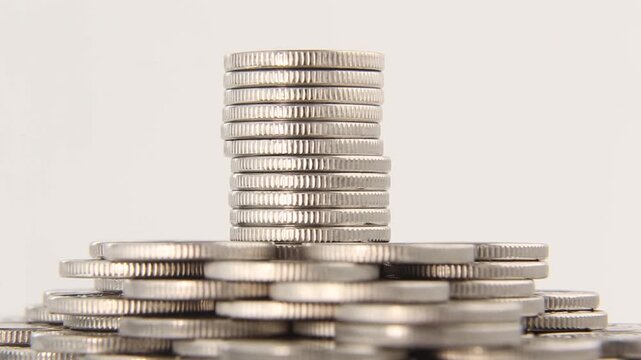 stacks of silver coins in a pile of coins arranged in a row on a light background in a seamless loop, the camera is held steady, showing wealth, savings and financial abundance. Looped video