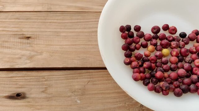 Hand picking fresh phalsa berries from plate on rustic wooden table