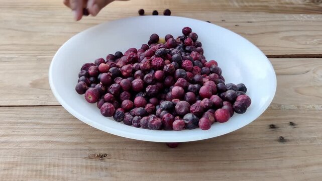 Person picking fallen falsa berries off wood surface putting in bowl