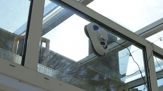 Automatic robot cleans a glass roof of a conservatory under bright sunlight.