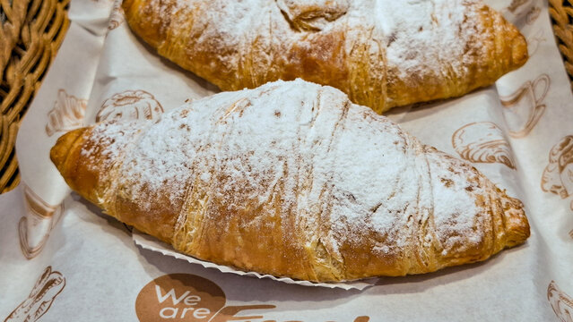 Freshly baked golden brown french croissants sprinkled with powdered icing sugar served on greaseproof paper in a bakery basket