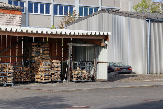 Brennholz in Gitterboxen neben einem Lagerschuppen