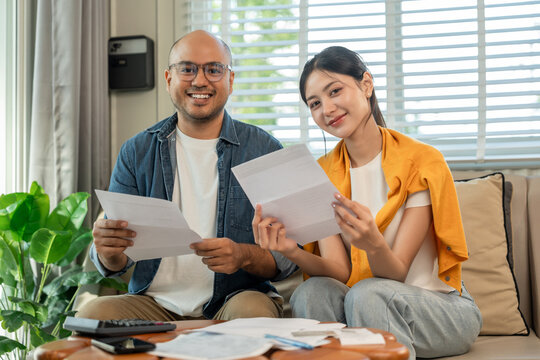 Young couple in the story begin their life together planning their future and managing finances and expenses. Happy Asian husband and wife calculating income and bills to plan for investment.