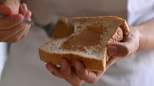 Woman hand spreading peanut butter on sliced whole wheat bread for breakfast