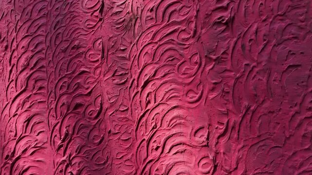 Abstract close-up shot panning along a vibrant pink textured concrete wall with swirling patterns under subtle afternoon shadows in a suburban recreational garden.
