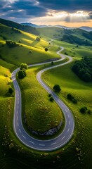 Obraz premium Winding road through rolling green hills with dramatic sunlight and shadows