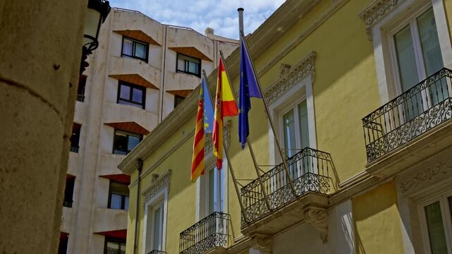 Flags of Spain, Valencia, and EU on a yellow building in Spain on a sunny day. dolly slide camera movement and slow motion