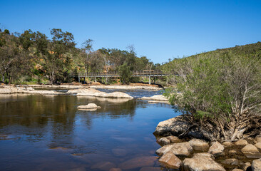 Fototapeta premium Wooden bridge over calm Swan River with rocky banks in Bells Rapids Park, Swan Valley, Western Australia, 25 September 2024