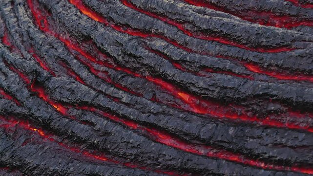 Extreme close-up of glowing magma visible through cracks in a cooling lava crust at Kīlauea Volcano, Hawaii. Flowing lava creates striking textures and patterns.