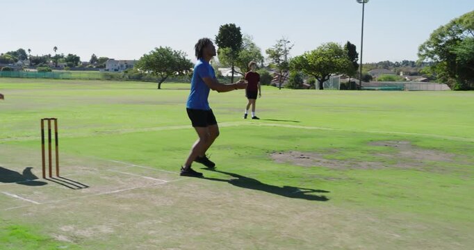 Batsman batting prompts male fielder moving behind stumps tracking ball flight on field