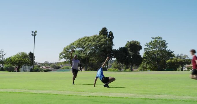 African american fielder diving, catching ball released by bowler, team celebrating in park