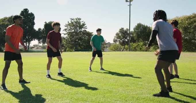Diverse male teammates reacting to trainer tossing ball, shuffling and passing for footwork
