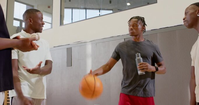 Diverse friends bouncing ball, passing bottles, gesturing after chatting at gym sideline