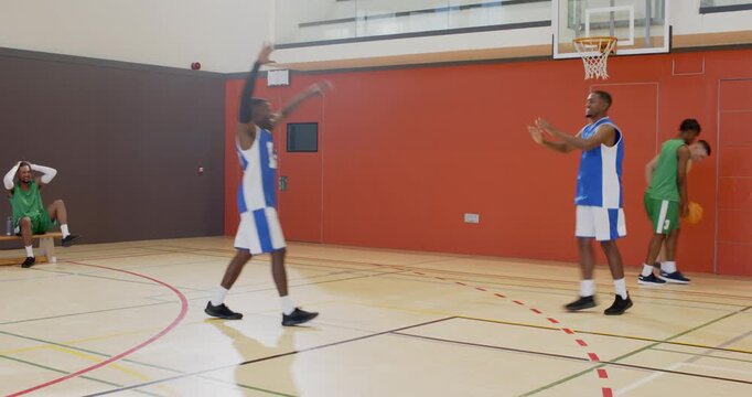 Defender closing baseline african american male duo dribbling, passing, jumping for layup at gym