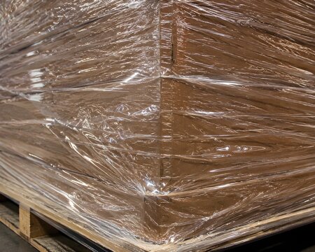 Macro shot industrial plastic shrink wrap tightly securing boxes pallet light glistening textured surface detail