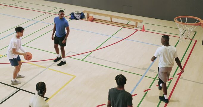 Diverse male palyers dribbling and shooting at hoop on court while taking turns practicing skills