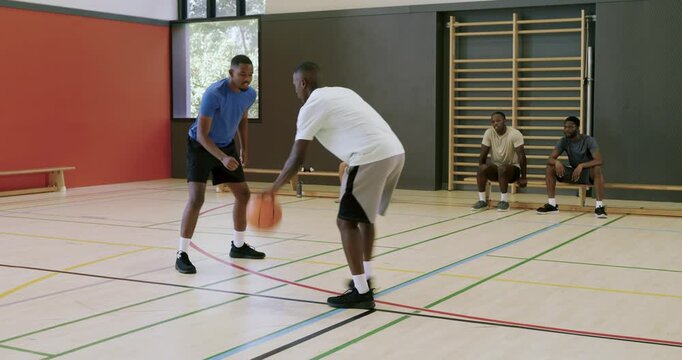 Man dribbling ball between-legs crossover after defender leaning to evade at gym