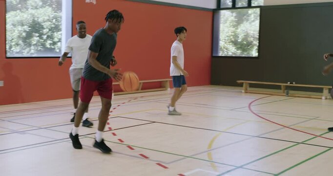 Diverse male athlete at gym slipping dribbling ball faking blue player driving toward basket