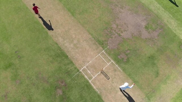 Teenage bowler running, ball at club ground, batsmen sprinting retrieving it to bowl