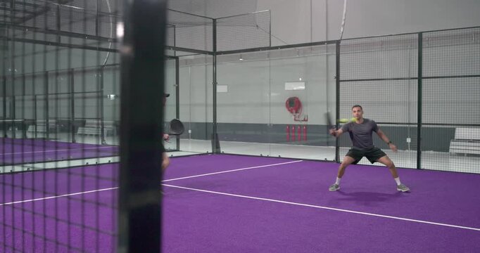 Two men practicing padel, tossing serve, volleying, bumping paddles on purple court