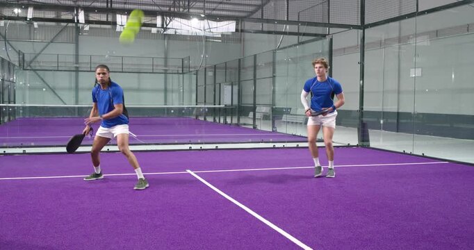 When teammate hitting ball, men volleying and smashing ball for rally on padel court