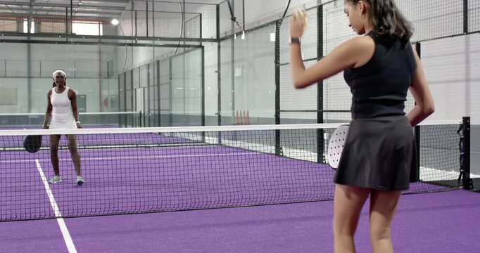 Diverse female competitors bouncing ball, serving underhand using paddles on purple tennis court