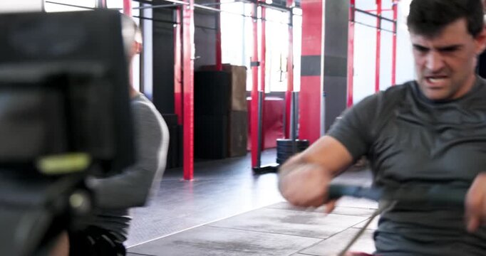 Entering gym, diverse male workout partners rowing on adjacent rowers in unison for sparring