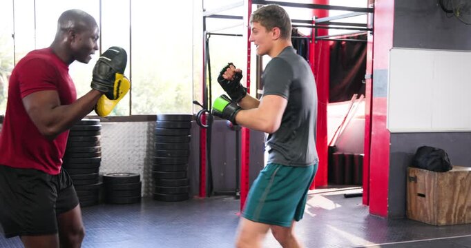 African american coach raising focus mitts, trainee throwing jab hooks in ring for timing drill