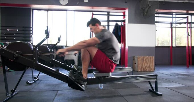Diverse male buddies at crossfit gym strapping feet adjusting grips rowing on machines, monitoring