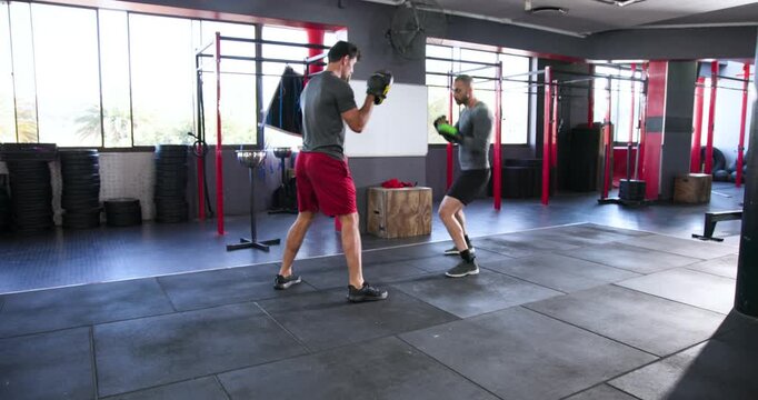 Trainer and trainee stepping, throwing jab-cross combos while trainee catching mitts at gym