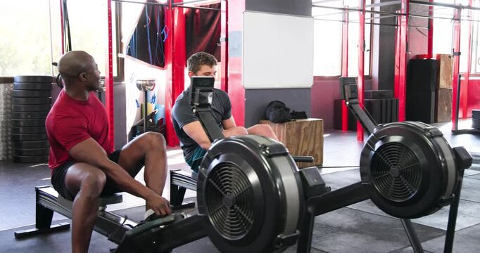 Diverse male training partners securing foot straps and rowing in sync for strength