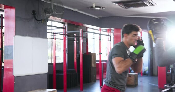 Diverse male partners training in gym, coach raising yellow focus mitts, trainee throwing combo