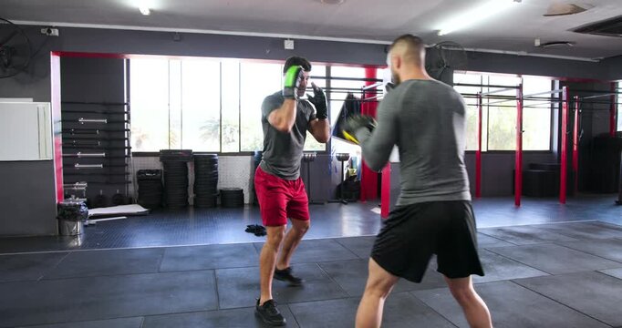White boxer with green gloves practicing combos as coach raising yellow mitts in gym