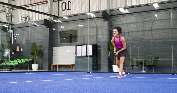 Hispanic female tracking lunging to hit ball, dribbling racket, returning on padel court