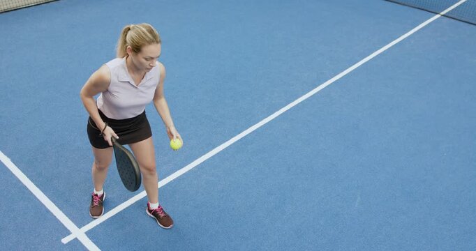 Female athlete bouncing ball to serve, tossing up, swinging paddle on court tracking flight