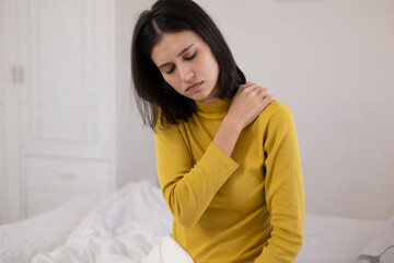 Naklejka premium The young woman sat on the bed. She felt pain and stiffness in her shoulders, neck, and back, along with muscle spasms and a general feeling of discomfort.