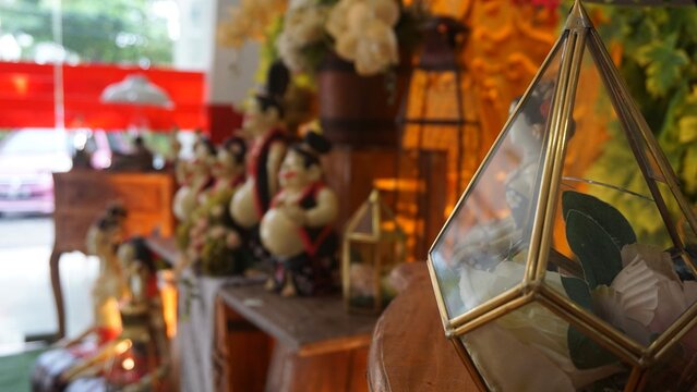 Close-up of a geometric glass terrarium prism on a wooden table with blurred Javanese statues in the background.