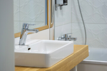Fototapeta premium modern bathroom sink with a chrome faucet on a light wood countertop in front of a white tiled wall and mirror