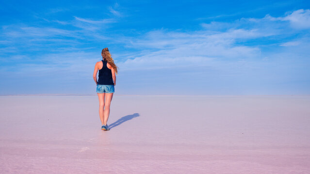 Minimalist back view of young woman walking alone in a pink salt flat desert under blue sky, authentic travel lifestyle photography expressing freedom and solitude